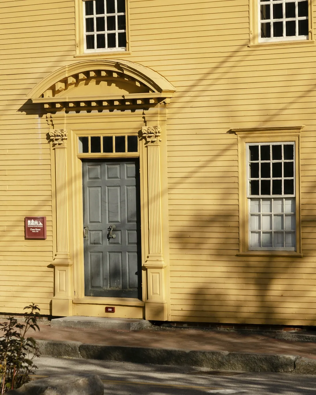 A colonial doorway with a carved pediment on a yellow clapboard house